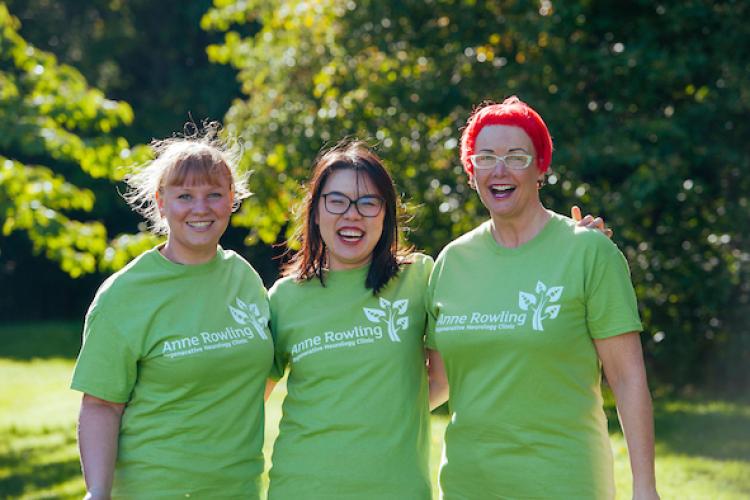3 people dressed in green Anne Rowling Clinic T-shirts linking arms and smiling