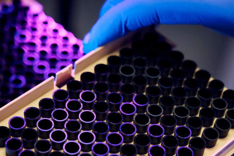 a hand wearing a blue glove picking up a 96-well laboratory sample plate