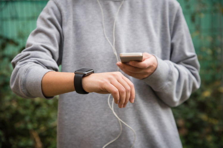 A person from the shoulders down holding a smart phone, and a wrist wearable device