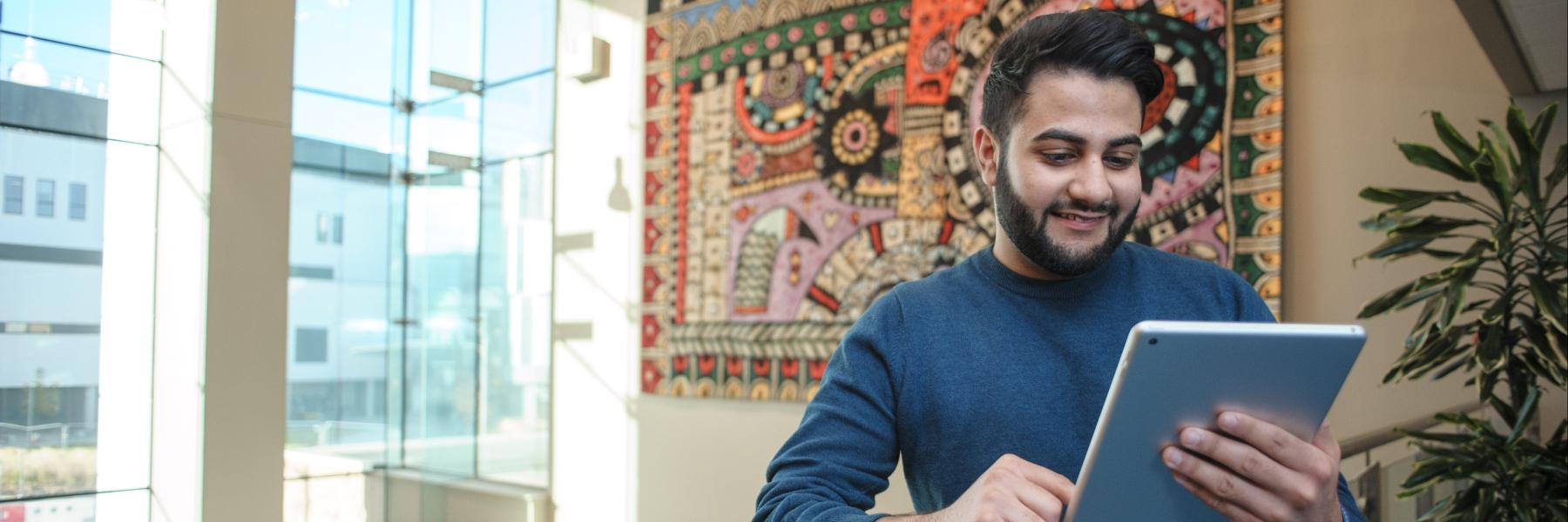 Man stood in front of window reading an electronic tablet