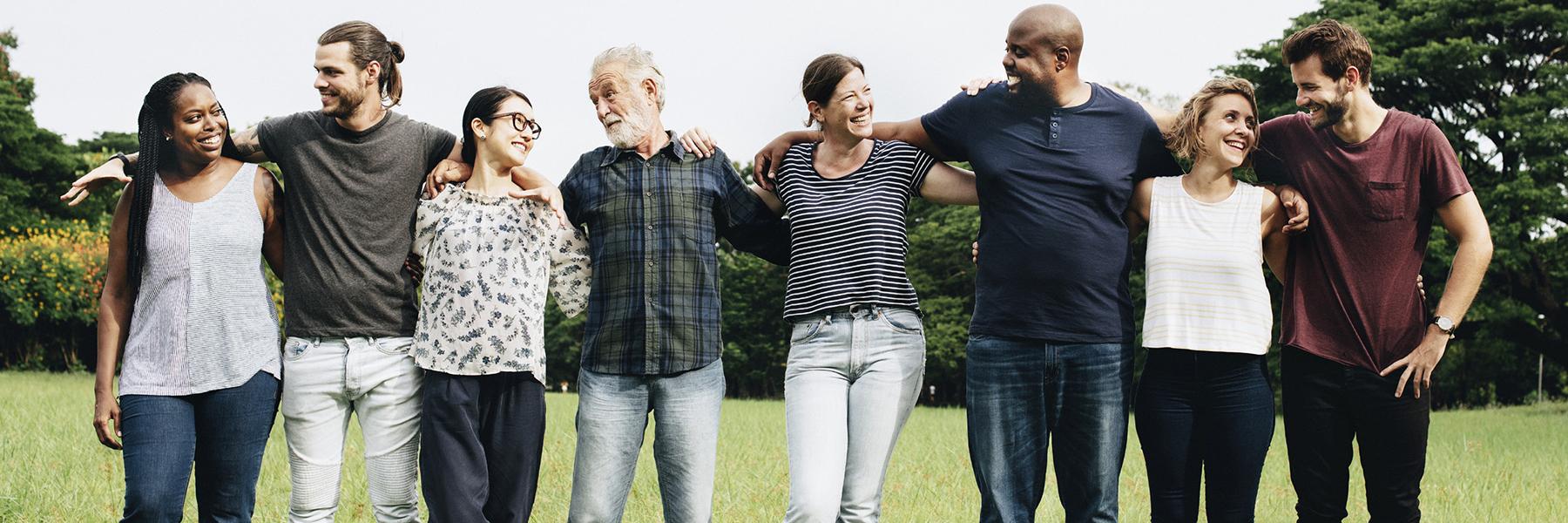 A group of happy people standing in a line outside with their arms around each other.
