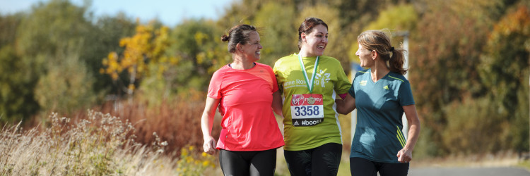 Three people pictured in running clothes, the person in the centre has an Anne Rwoling Clinic running t-shirt on and a participation medal and a running number