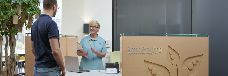 A receptionist wearing NHS uniform is greeting a patient at the Clinic front desk