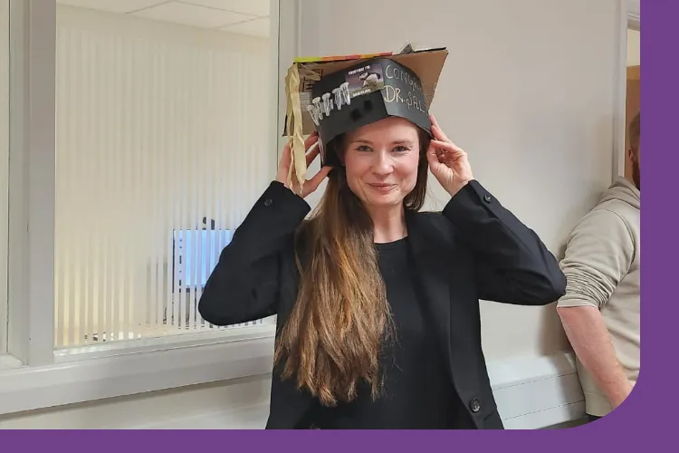 Dr Andrea Salzinger smiling and wearing a home-made graduation hat